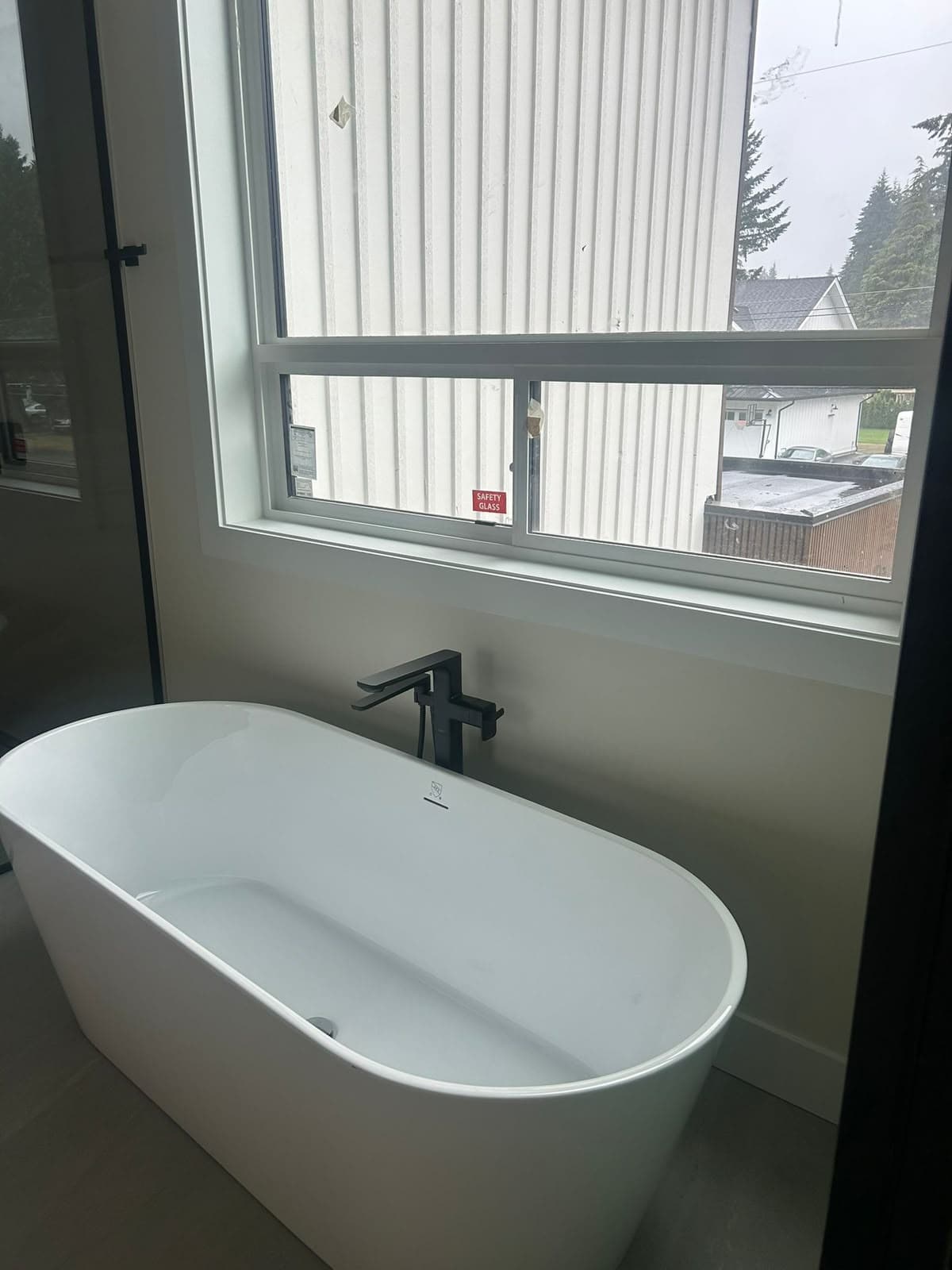 Freestanding bathtub with a matte black floor-mounted filler under a window